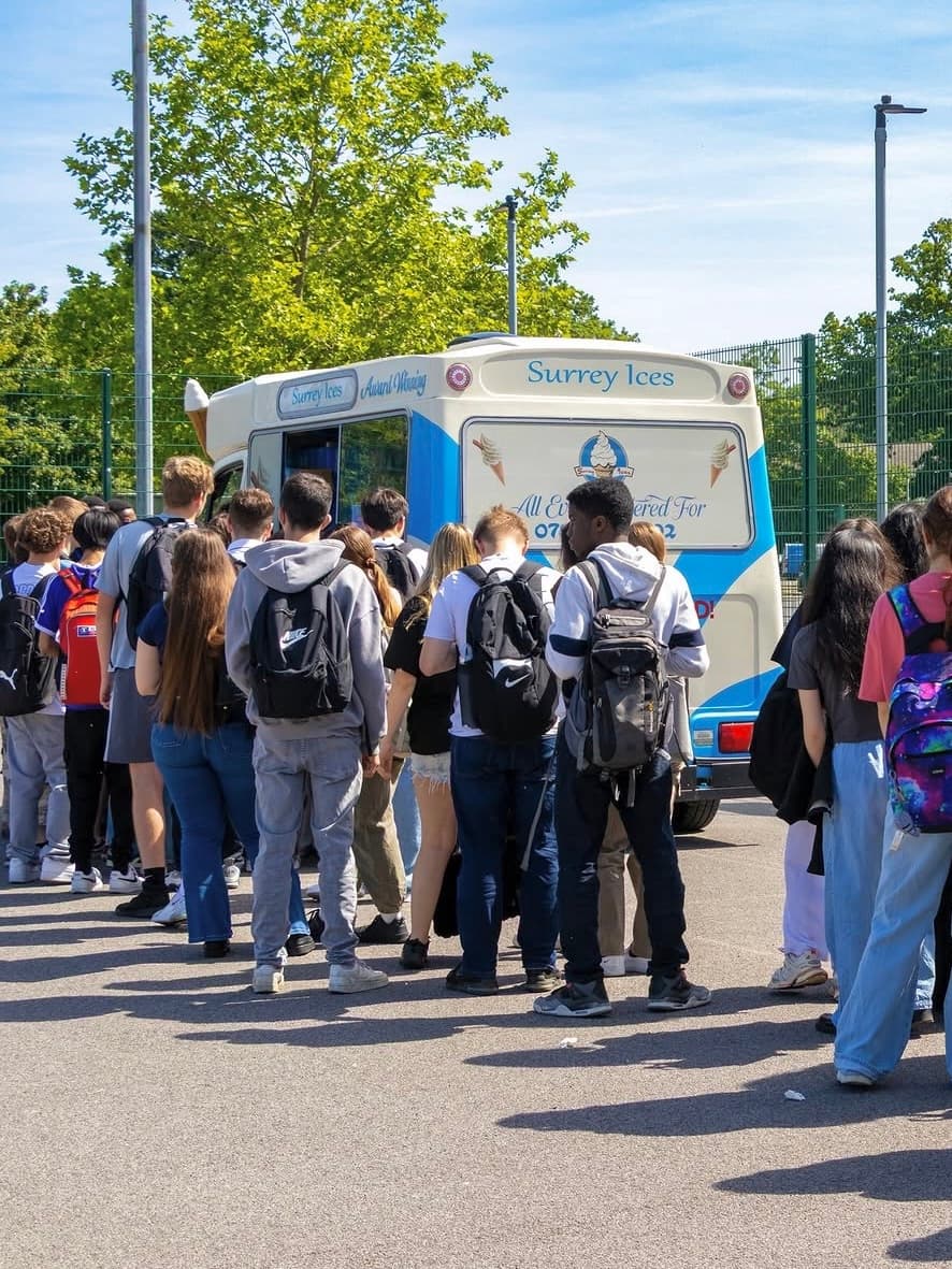 A queue of people waiting at a blue and cream Surrey Ices van