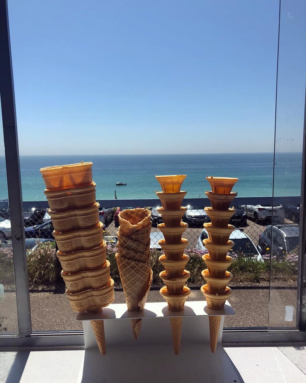 Stacks of ice cream cones on a windowsill, with the sea visible through the glass