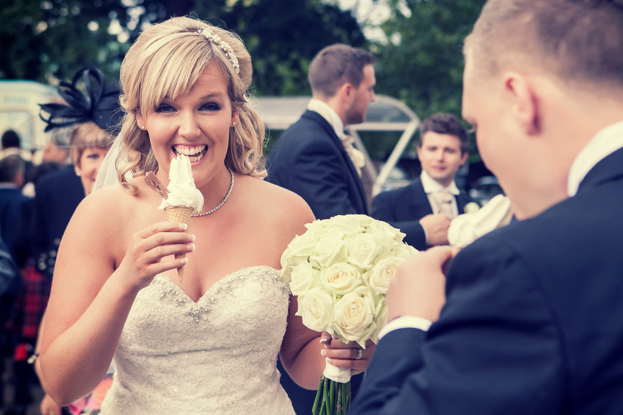 A bride in a white gown smiling with a soft serve cone and a bouquet of white roses